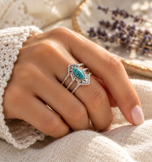 Close-up lifestyle image of a woman's hand wearing the Spirit of Serenity stainless steel adjustable ring, featuring an oval turquoise-inspired stone and intricate silver-tone detailing, resting on cream linen fabric.