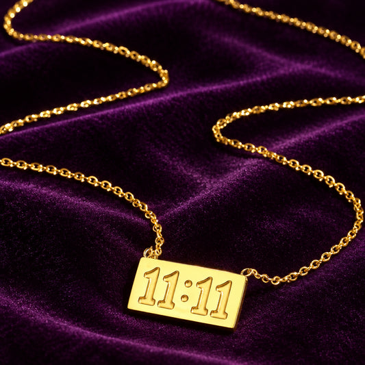 Gold Divine Timing 11:11 stainless steel necklace with rectangular angel number pendant and delicate chain displayed on deep purple velvet.