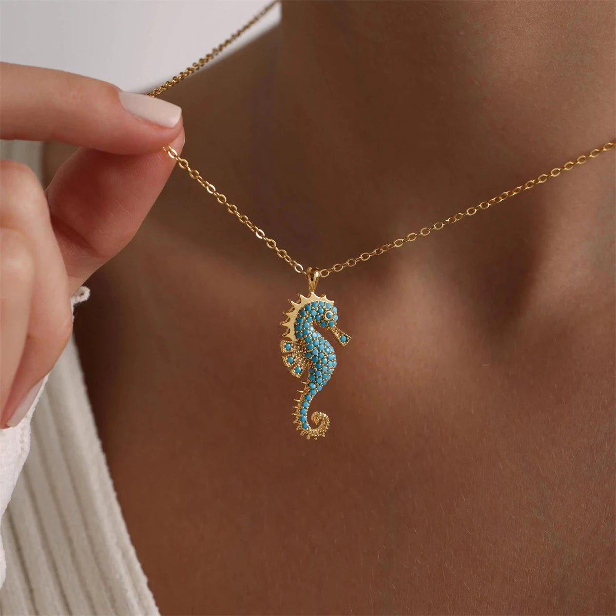 Close-up of Ocean's Guardian Seahorse Necklace in 18K gold-plated stainless steel with turquoise-coloured zircon details, worn around the neck with a hand gently holding the chain.