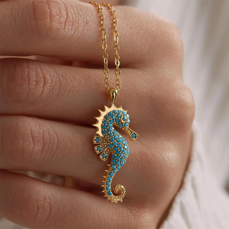 Close-up of Ocean's Guardian Seahorse Necklace in 18K gold-plated stainless steel with turquoise-coloured zircon details, displayed against a hand.