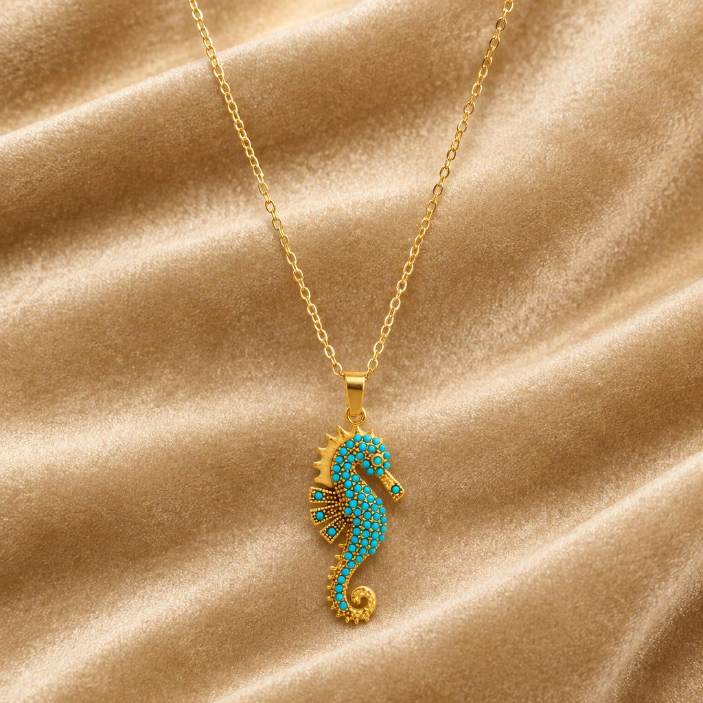 Ocean's Guardian Seahorse Necklace in 18K gold-plated stainless steel, featuring a turquoise-coloured zircon seahorse pendant and delicate gold chain displayed on champagne Velvet.