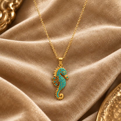 Ocean's Guardian Seahorse Necklace in 18K gold-plated stainless steel, featuring a turquoise-coloured zircon seahorse pendant and delicate gold chain displayed on champagne velvet.