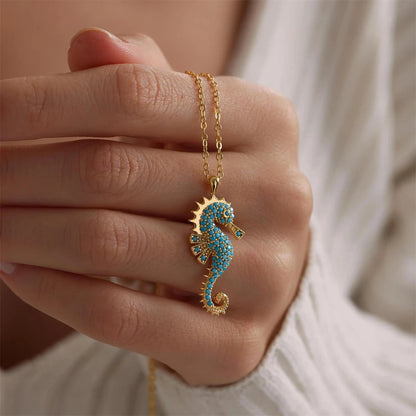 Close-up of Ocean's Guardian Seahorse Necklace in 18K gold-plated stainless steel with turquoise-coloured zircon details, displayed against a hand.